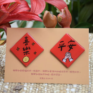 喜樂平安春聯磁鐵組實拍圖,兩枚紅色菱形磁鐵展示「喜樂」與「平安」字樣,搭配民數記6章24至26節經文卡與花卉背景。