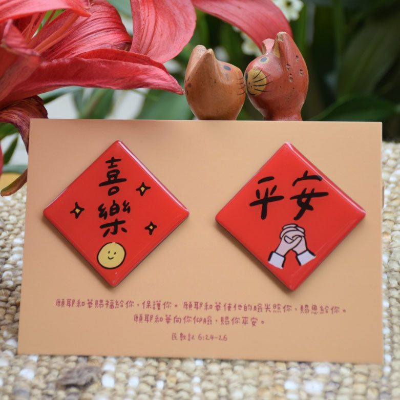喜樂平安春聯磁鐵組實拍圖,兩枚紅色菱形磁鐵展示「喜樂」與「平安」字樣,搭配民數記6章24至26節經文卡與花卉背景。