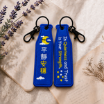 平靜藍色瓶安同行刺繡吊飾雙面展示,一面為中文「平靜安穩」字樣,另一面為英文 In Quietness and Trust is Your Strength. 字樣,搭配月亮、雲朵與星星刺繡及黑色掛鉤。