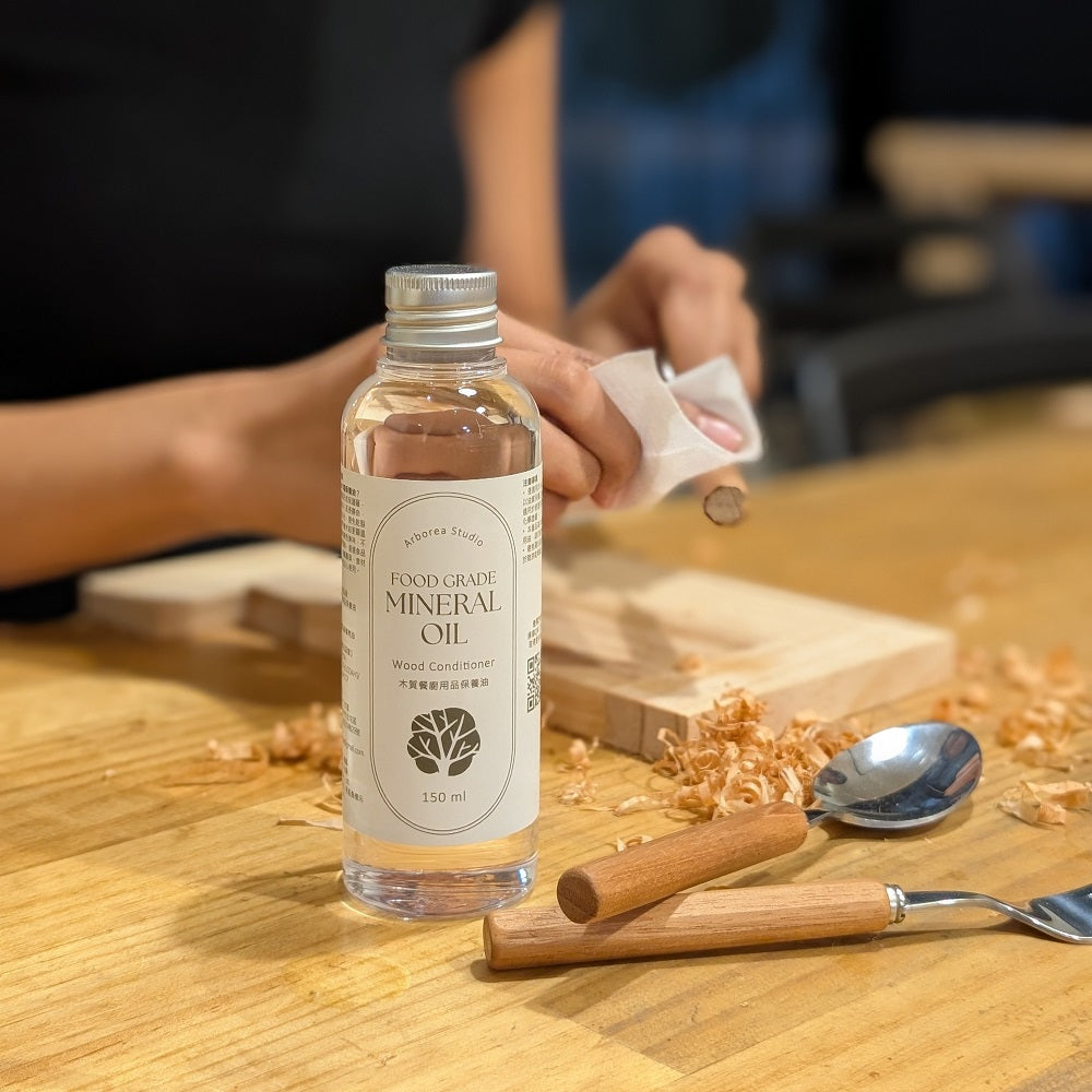 Arborea 食品級木器保養油 150mL 使用情境,保養油放置於木工作業桌面,旁邊展示木製餐具、木屑與木器擦拭作業