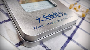 《天父樂愛你》音樂恩典卡銀色收納鐵盒近拍,展示金屬表面質感、透明視窗及藍色「天父樂愛你」中英文標誌。