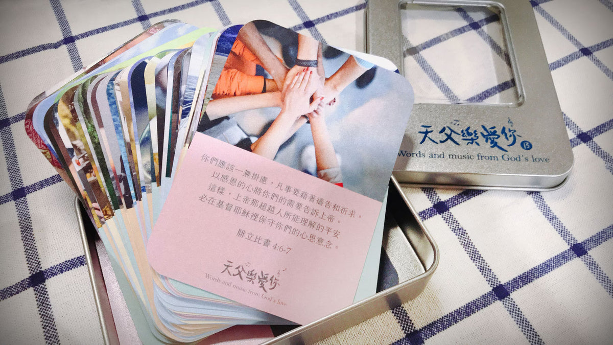 《天父樂愛你》音樂恩典卡 B 款實拍,多張彩色圖卡展開於銀色鐵盒中,前方粉紅色卡片呈現多人雙手交疊照片及腓立比書4章6至7節經文。