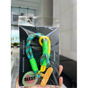 綠黃 BLESS 款手機短掛繩包裝展示，藍綠編織繩搭配亮綠與黃色纏繩、手機夾片及 BLESS 圓形吊牌。