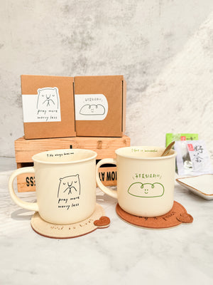 生命的糧陶瓷杯情境圖，淺米色陶瓷杯與同系列商品、包裝盒及杯墊一同陳列於桌面上，杯身正面印有「每早晨都是新的」與綠色線條笑臉圖案。