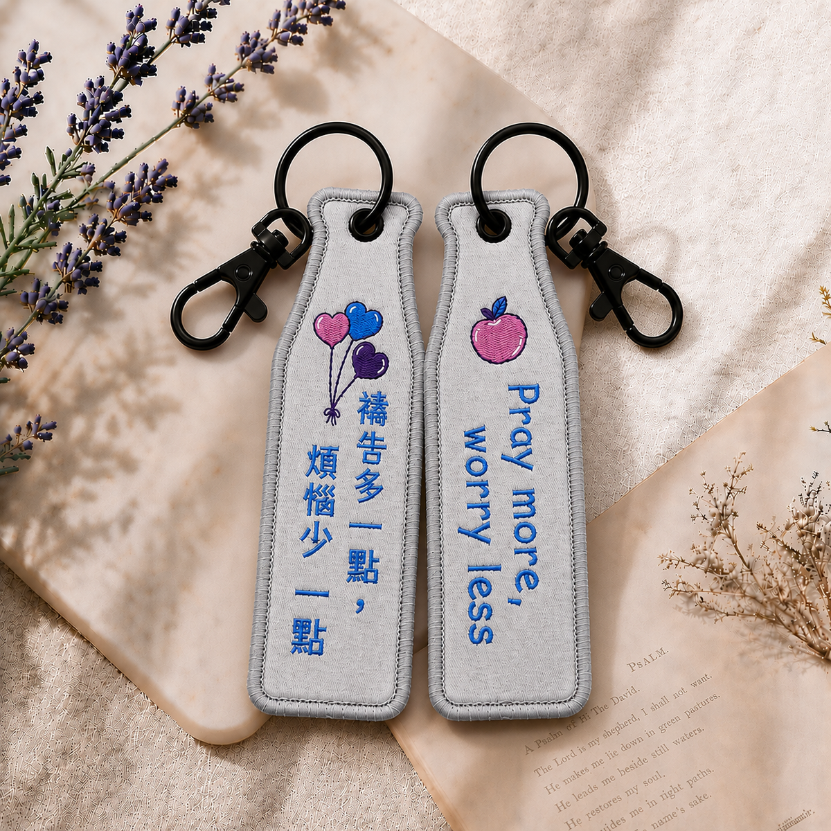禱告灰色瓶安同行刺繡吊飾雙面展示，一面為中文「禱告多一點，煩惱少一點」字樣，另一面為英文 Pray more, worry less 字樣，搭配愛心氣球與蘋果刺繡圖案及黑色掛鉤。