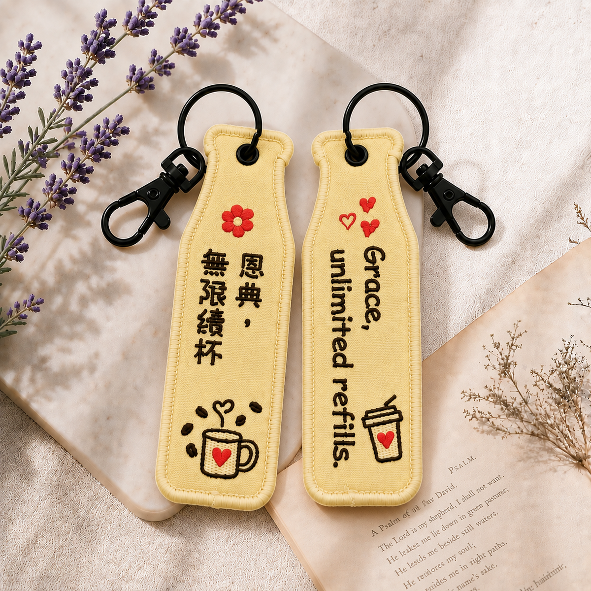 恩典黃色瓶安同行刺繡吊飾雙面展示，一面為中文「恩典・無限續杯」字樣，另一面為英文 Grace, unlimited refills. 字樣，搭配花朵、愛心杯插畫及黑色掛鉤。