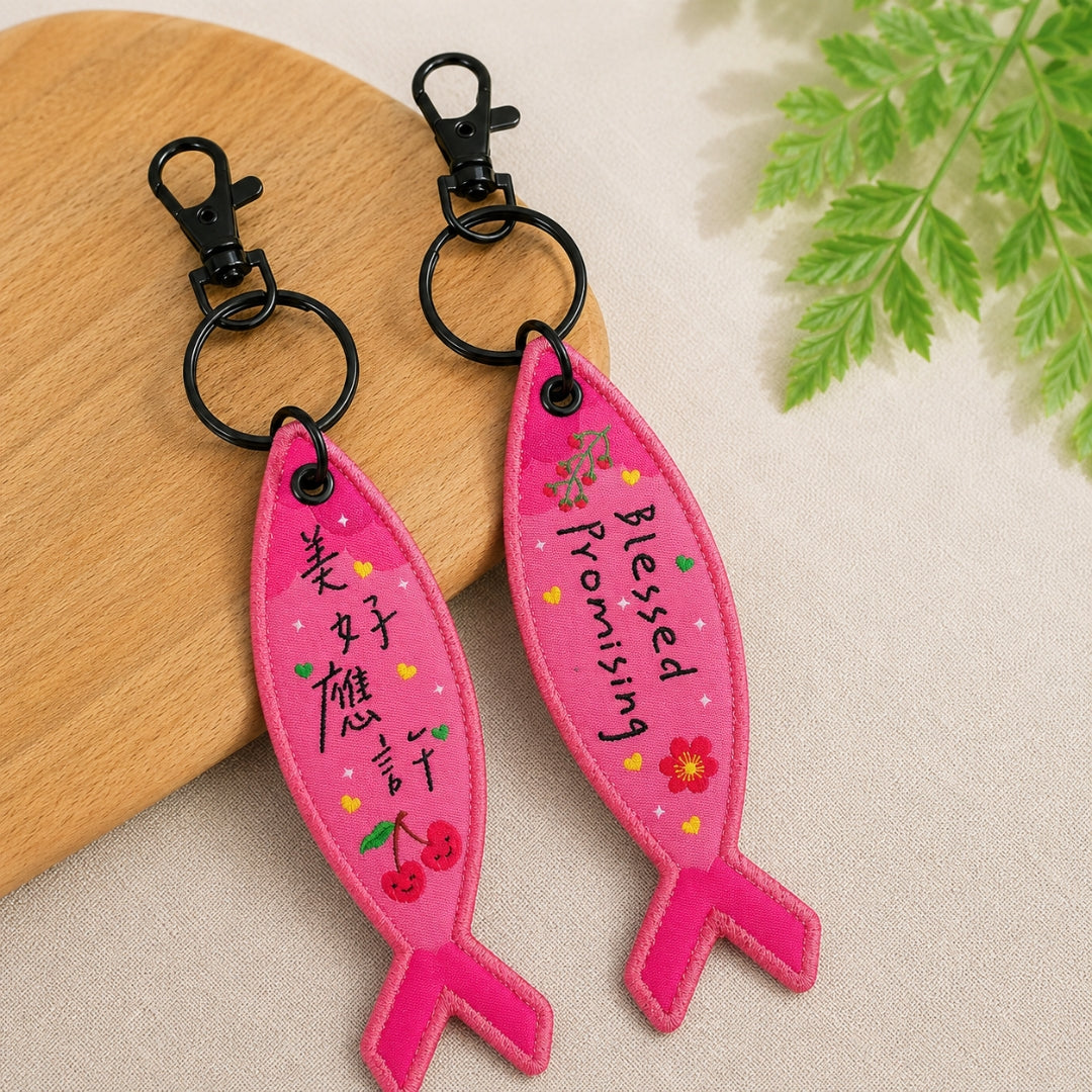 美好應許粉色得人如魚吊飾雙面展示，魚形彩織吊飾分別呈現中文「美好應許」與英文 Blessed Promising 字樣，附黑色掛鉤。